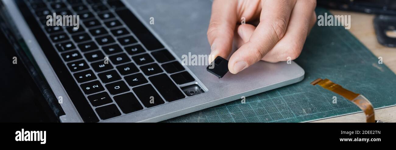 Cropped view of repairman holding broken key of keyboard near laptop at workplace, banner Stock Photo