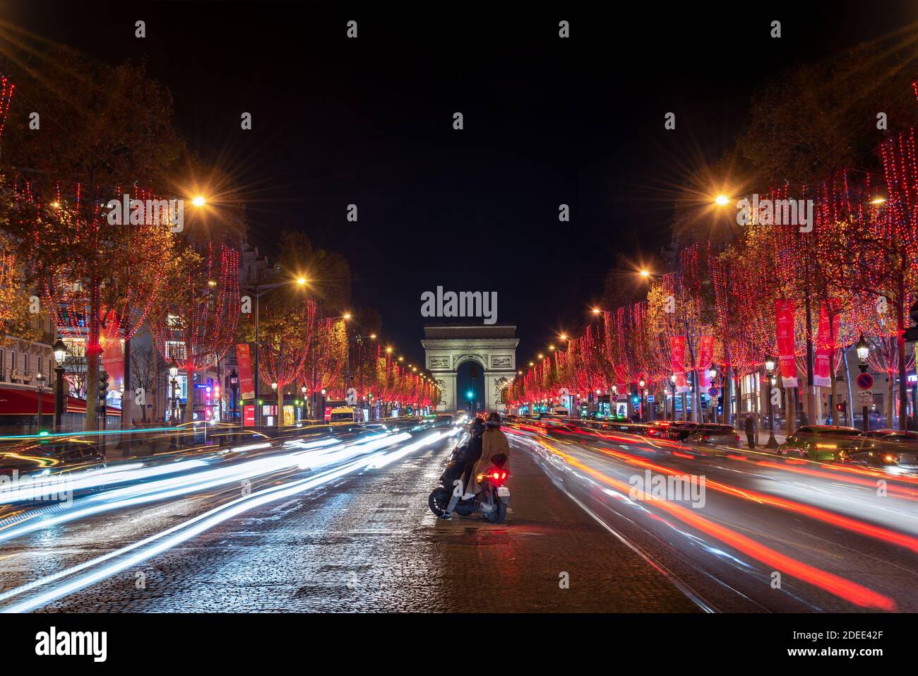 Young couple on Champs Elysees avenue and the Arc de Triomphe decorated with red Christmas lights at night  in Paris, France. Christmas holidays, wint Stock Photo