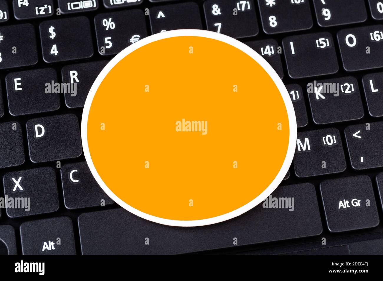Single empty orange circle label logo space, round symbol blank sticker laying on black modern pc laptop netbook computer keyboard, closeup, copyspace Stock Photo