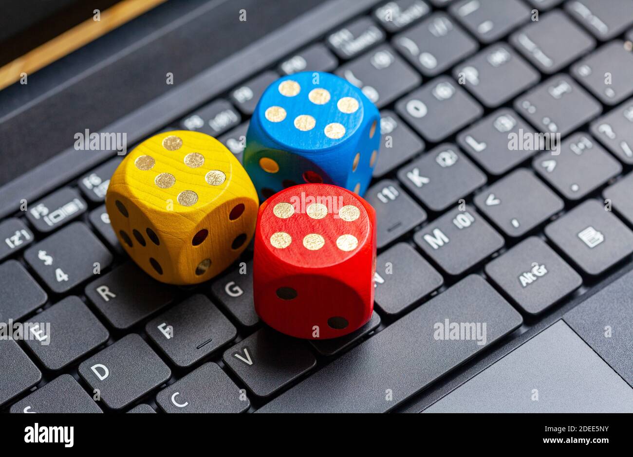 Three colorful wooden game dice showing six laying on a modern laptop
