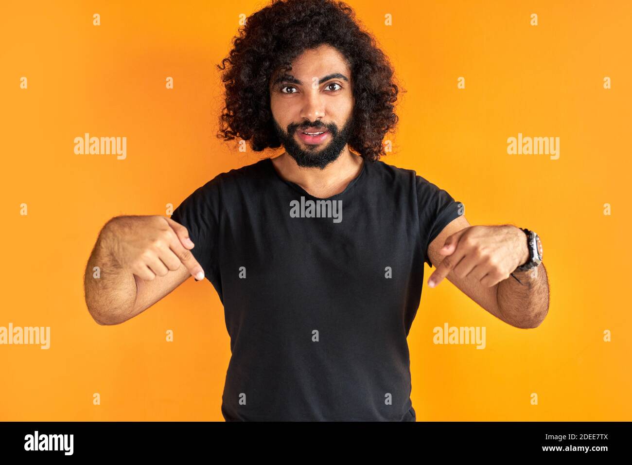 serious cury man points down with index finger, dressed in casual clothes, shows free space for your advertising content Stock Photo
