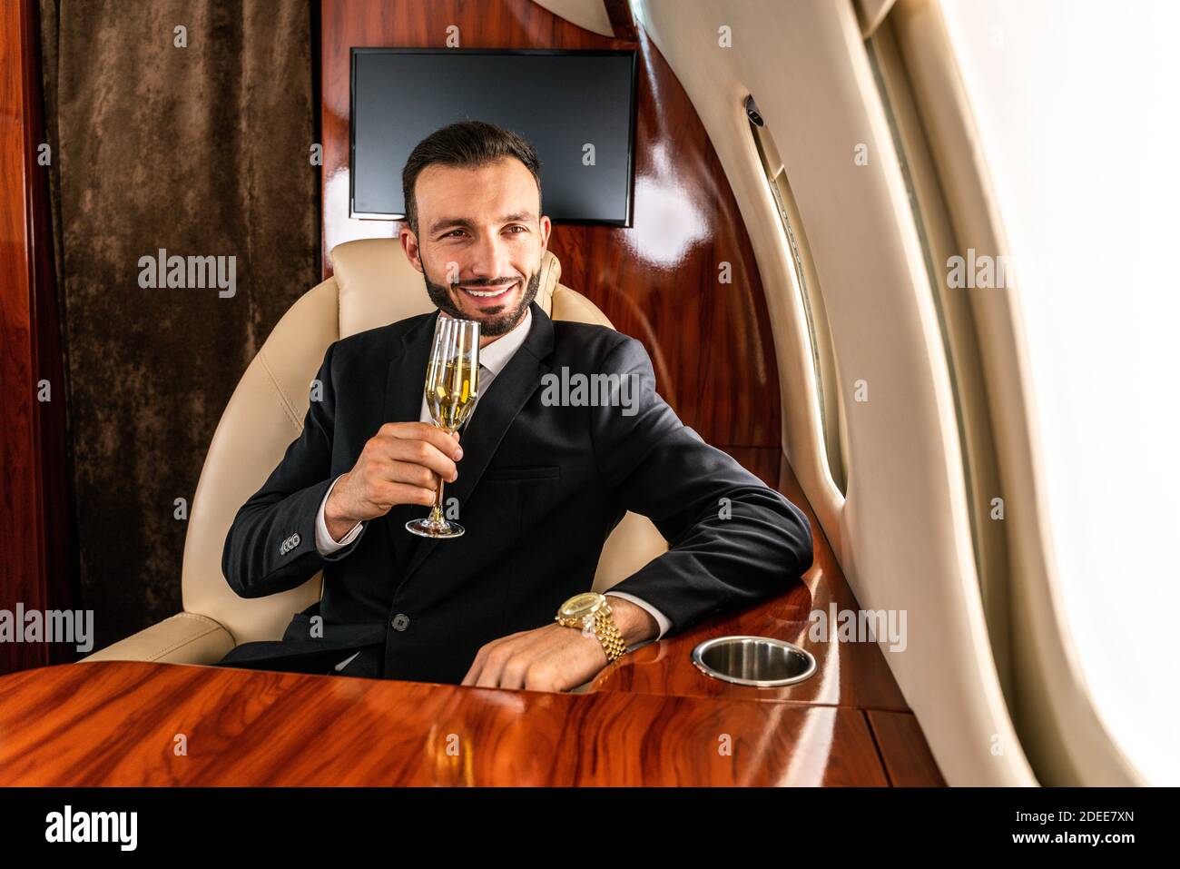 Handsome businessman wearing elegant suit  flying on exclusive private jet - Successful entrepreneur sitting in exclusive business class on airplane, Stock Photo