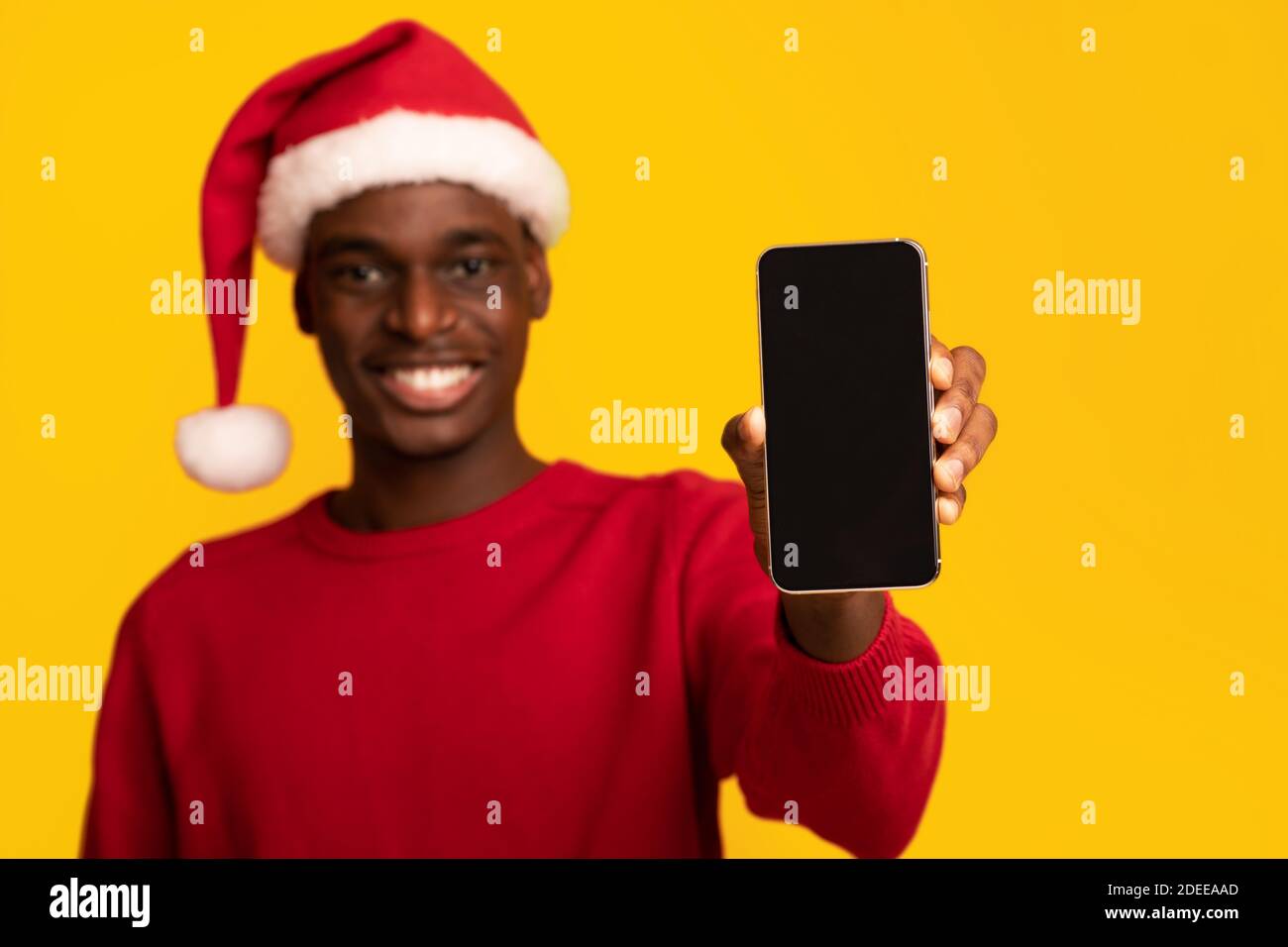 Mockup Of African Guy In Santa Hat Holding Smartphone With Black Screen Stock Photo