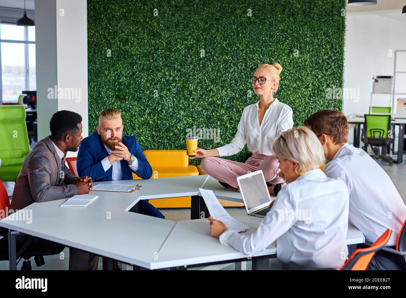 female office worker is meditating, taking break at work for mental balance while others work. mindful businesswoman feeling relief and no stress doin Stock Photo