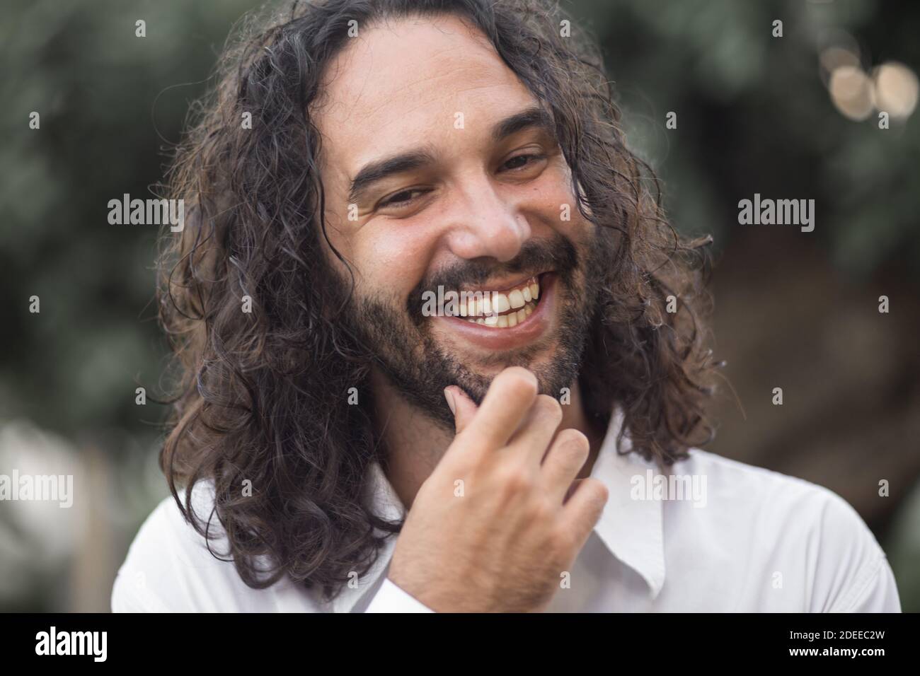 A young Hispanic bearded man with long hair posing at the camera outdoors Stock Photo