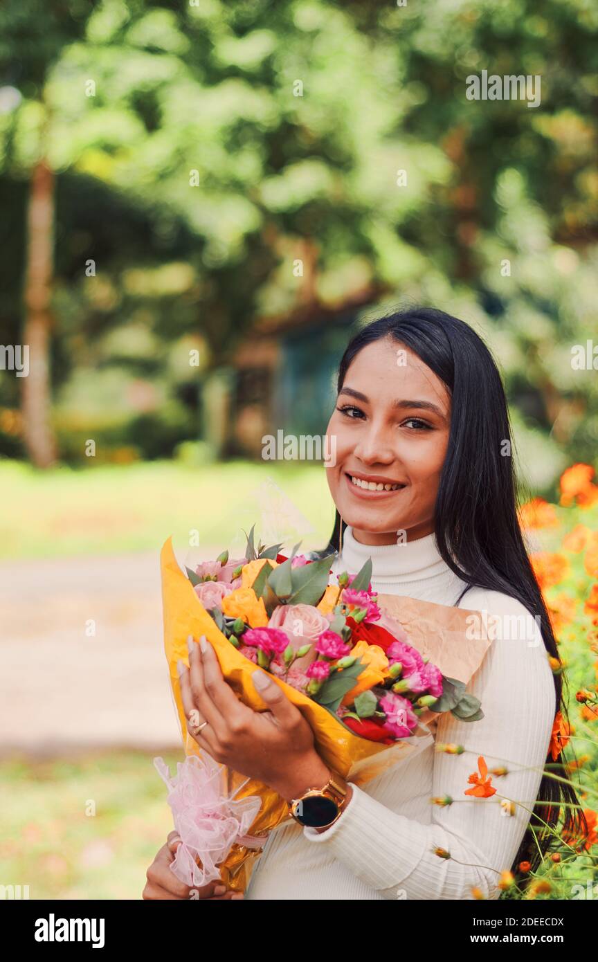 A happy young woman holding a bouquet of roses and standing next to a ...