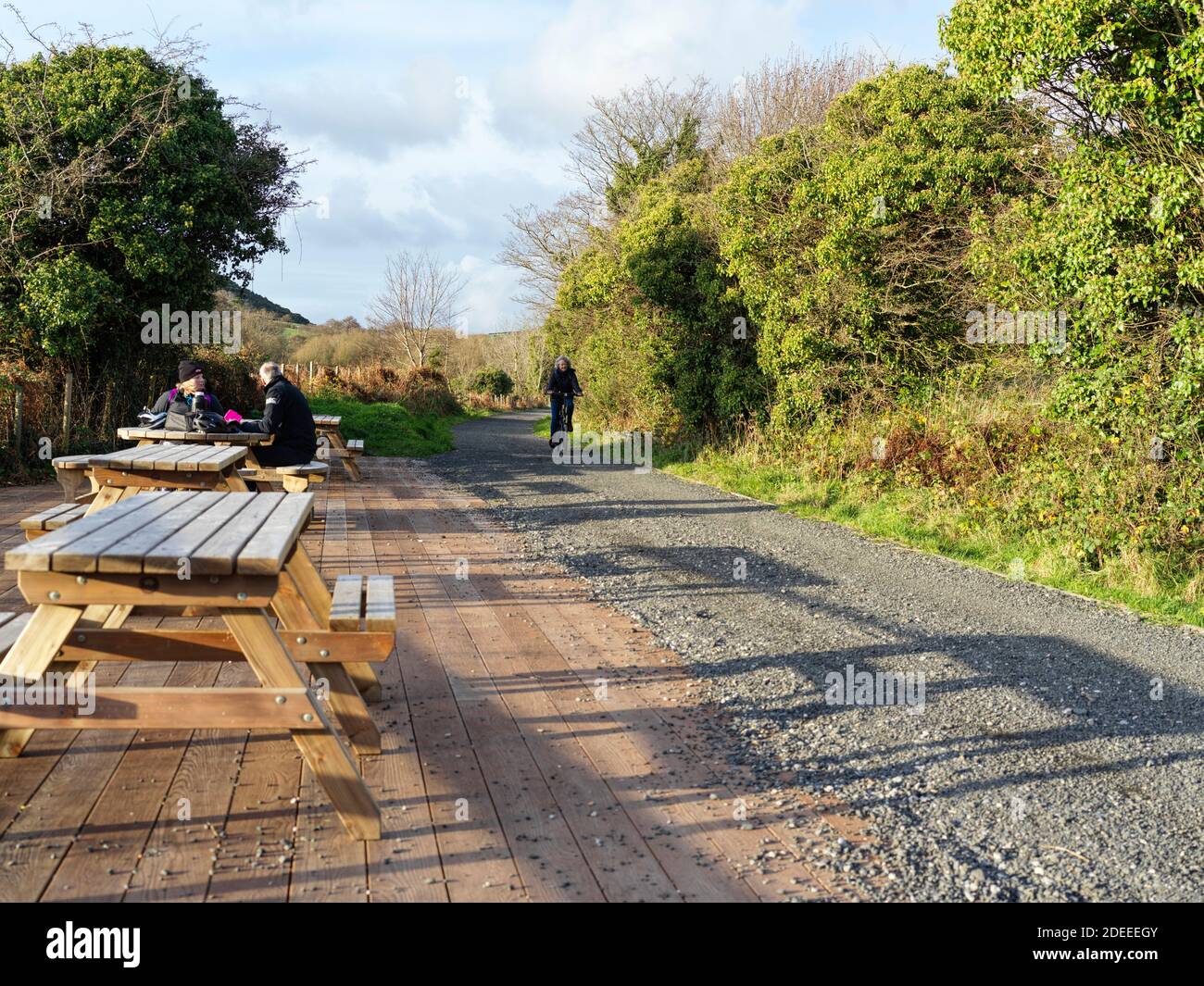 A cyclist on the Peel to Douglas long distance cycle path that follows the disused railway line passes the halfway mark where a stopping area has been Stock Photo