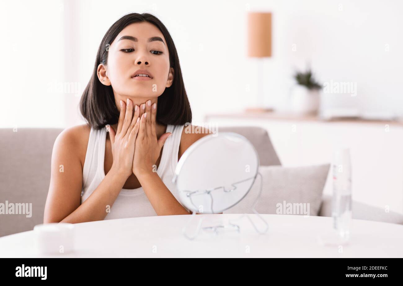 Young asian woman massaging her neck looking in the mirror Stock Photo ...