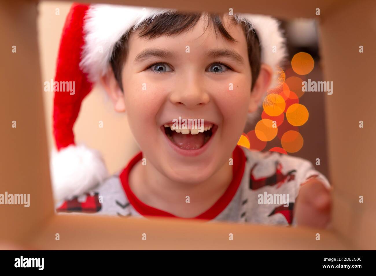 A happy, handsome Caucasian boy in a New Year's jumper and a Santa Claus hat smashes into a box Stock Photo
