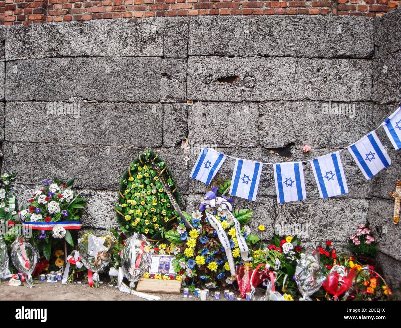 Flowers and wreaths lay at The Death Wall at the Auschwitz Concentration and Exteerminaton Camp. Located in the yard at the side of Block 11 Stock Photo