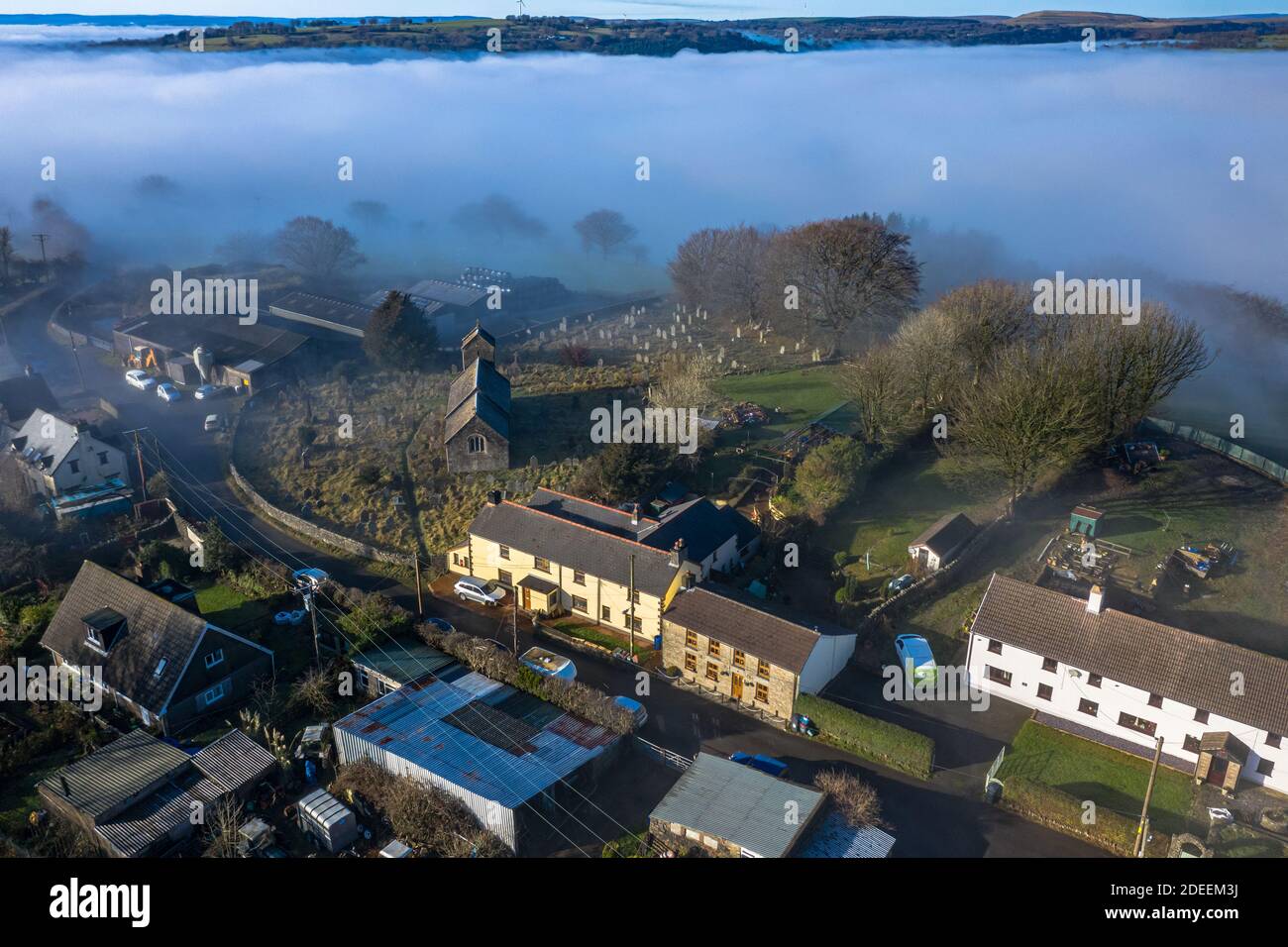 Beautiful morning of drone footage overlooking welsh sceneray small village with fog sheet covering the lower valleys in south wales uk. Stock Photo