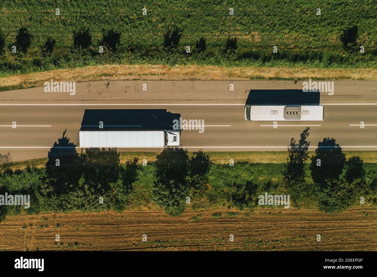 Truck and bus on the road from drone pov, top view of two vehicles passing by each other on roadway through countryside Stock Photo