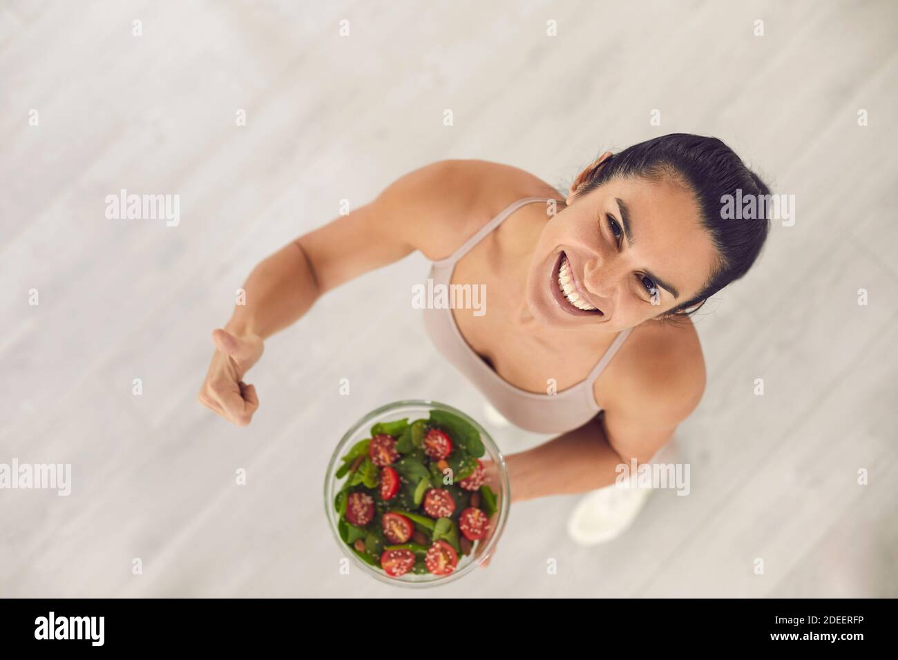 Fit woman holding bowl of vegetable salad, giving thumbs-up and smiling at camera Stock Photo