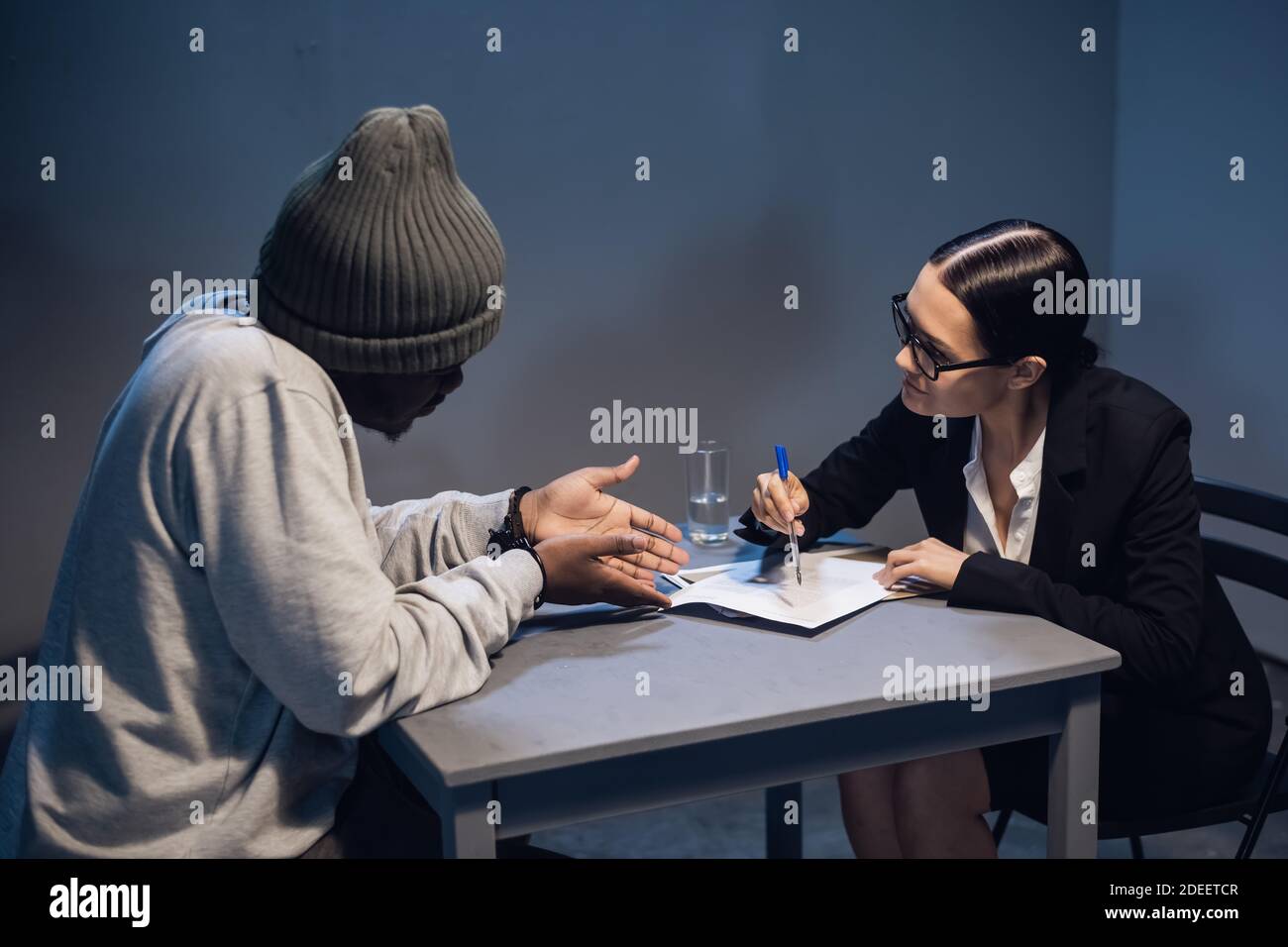A black criminal in a hat communicates with his lawyer at the table in