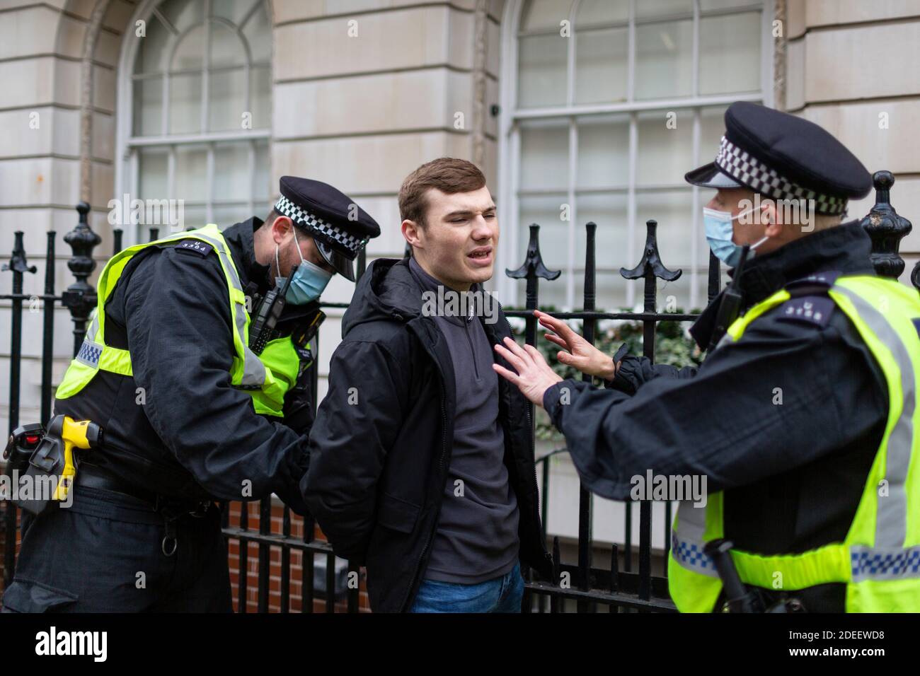 Anti-lockdown protest, London, 28 November 2020. A young man is arrested by police officers on a sidewalk. Stock Photo