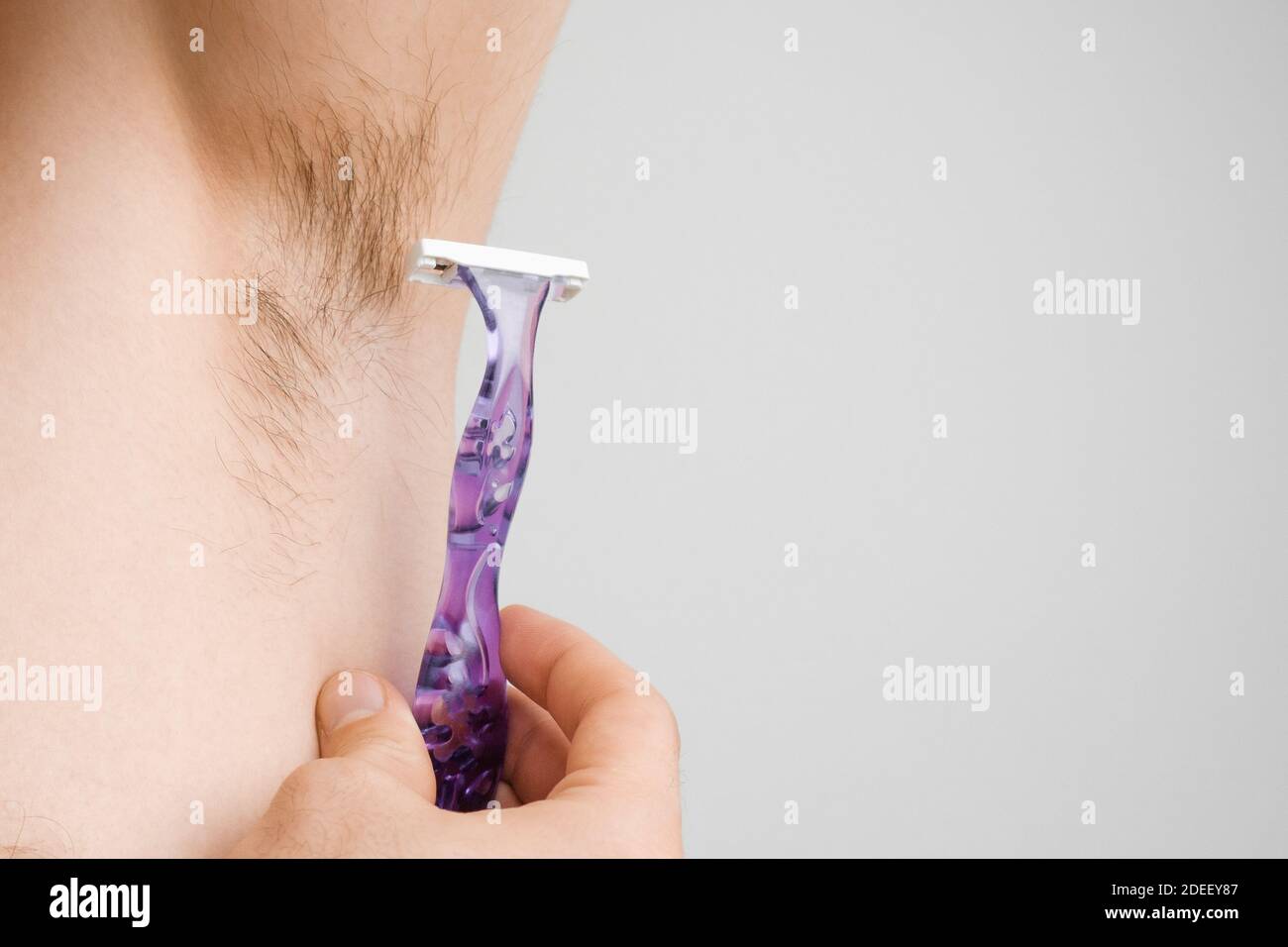 Close up man shaves hairy armpits with a purple razor. Unshaved armpits or underarm. Depilation and hair remove procedure Stock Photo