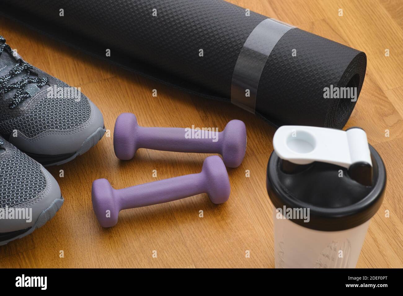 Protein shaker, dumbbells, sport shoes and exercise mat on the floor. Close up. Stock Photo