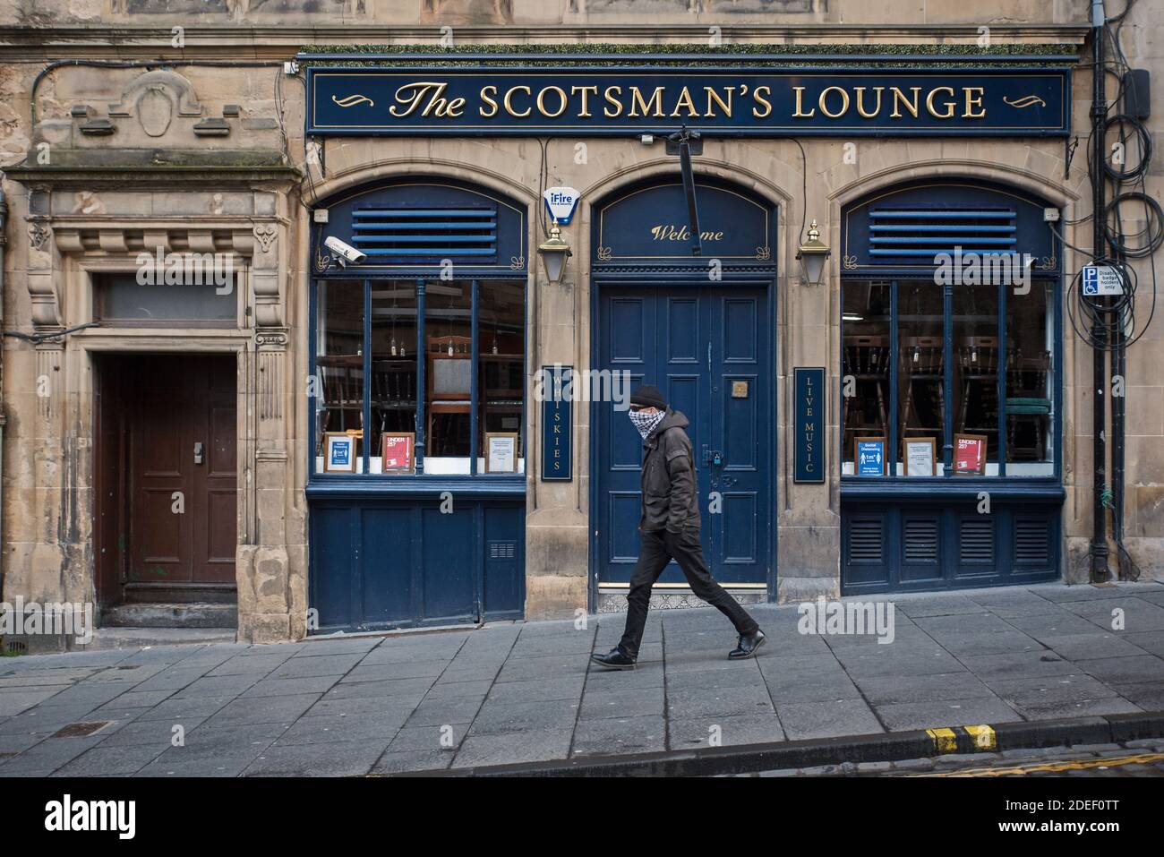 Man with a face mask walking past a public house closed because of