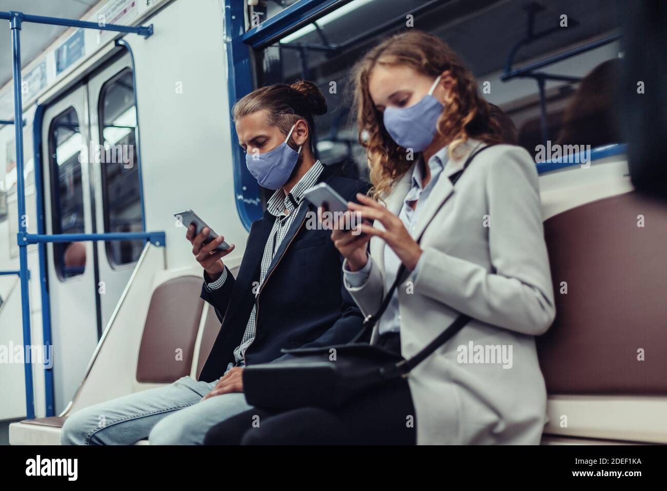 passengers wearing protective masks using their smartphones while sitting in a subway car. Stock Photo