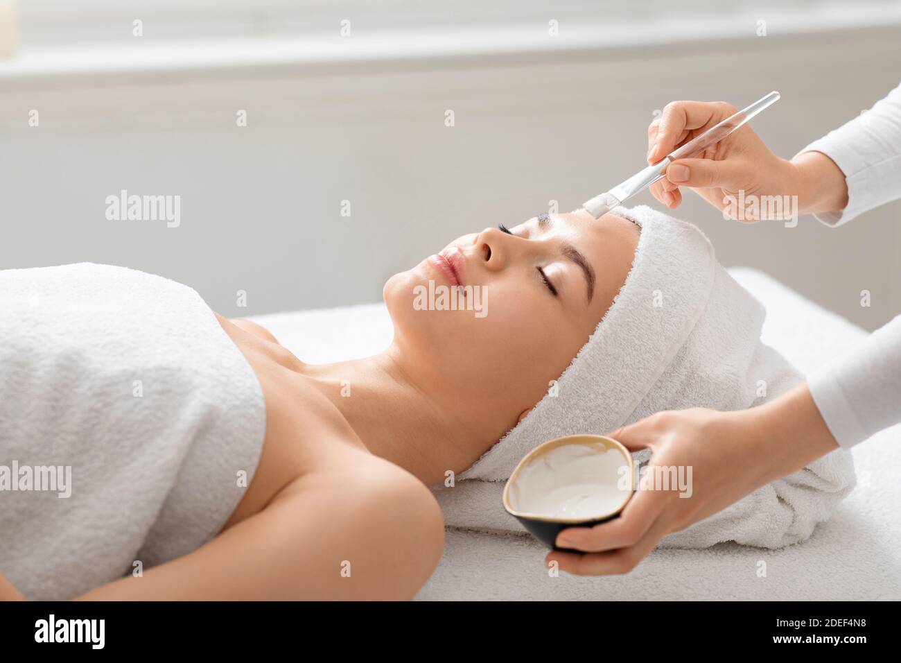Unrecognizable spa attendant applying clay mask on sleeping lady face Stock Photo
