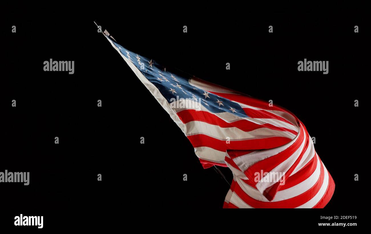 American flag blowing in the wind isolated against a black background. Symbol of North America Stock Photo