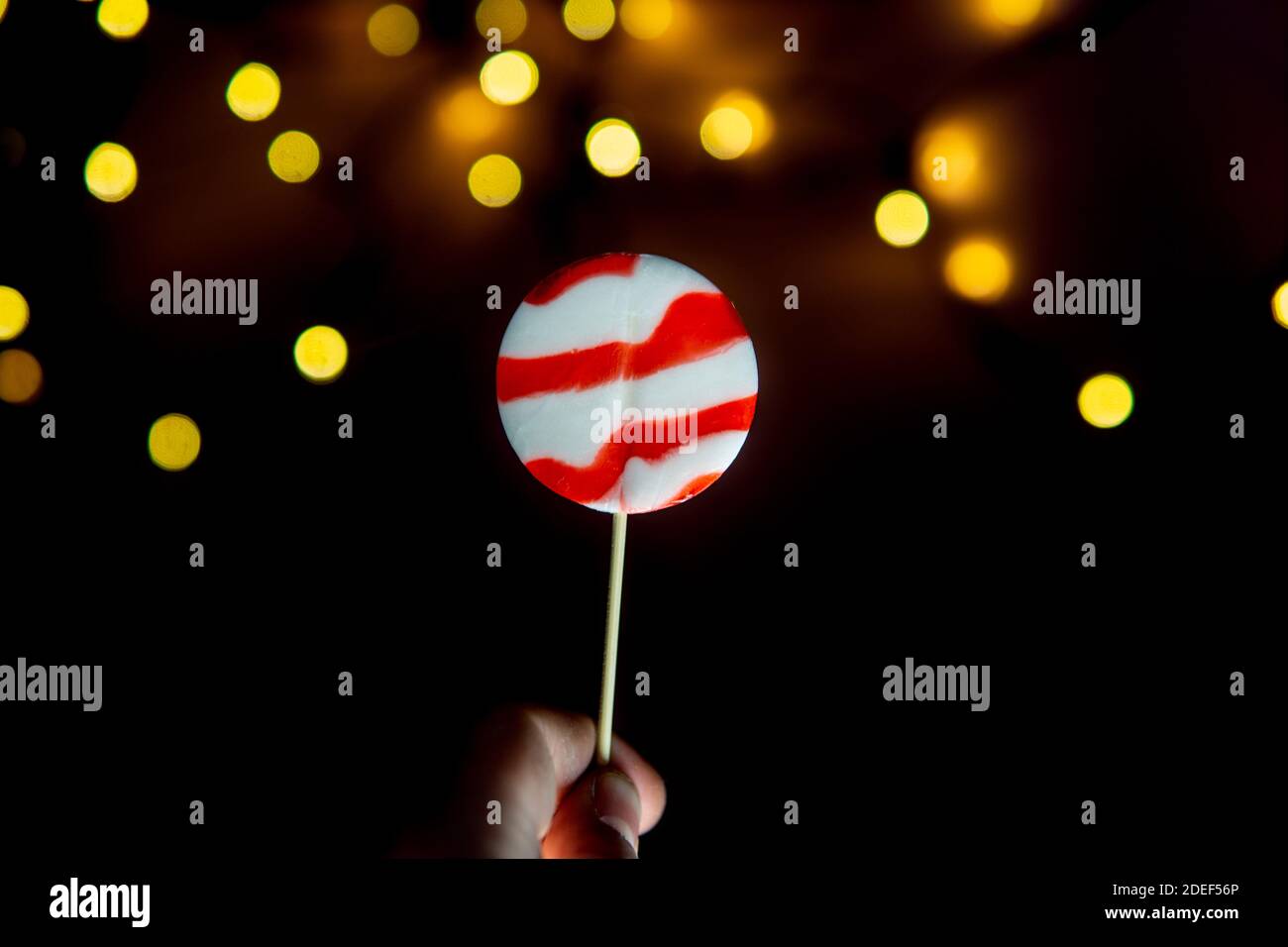Red and white lollipop in hand in front of light bubbles. Minimal Christmas concept Stock Photo