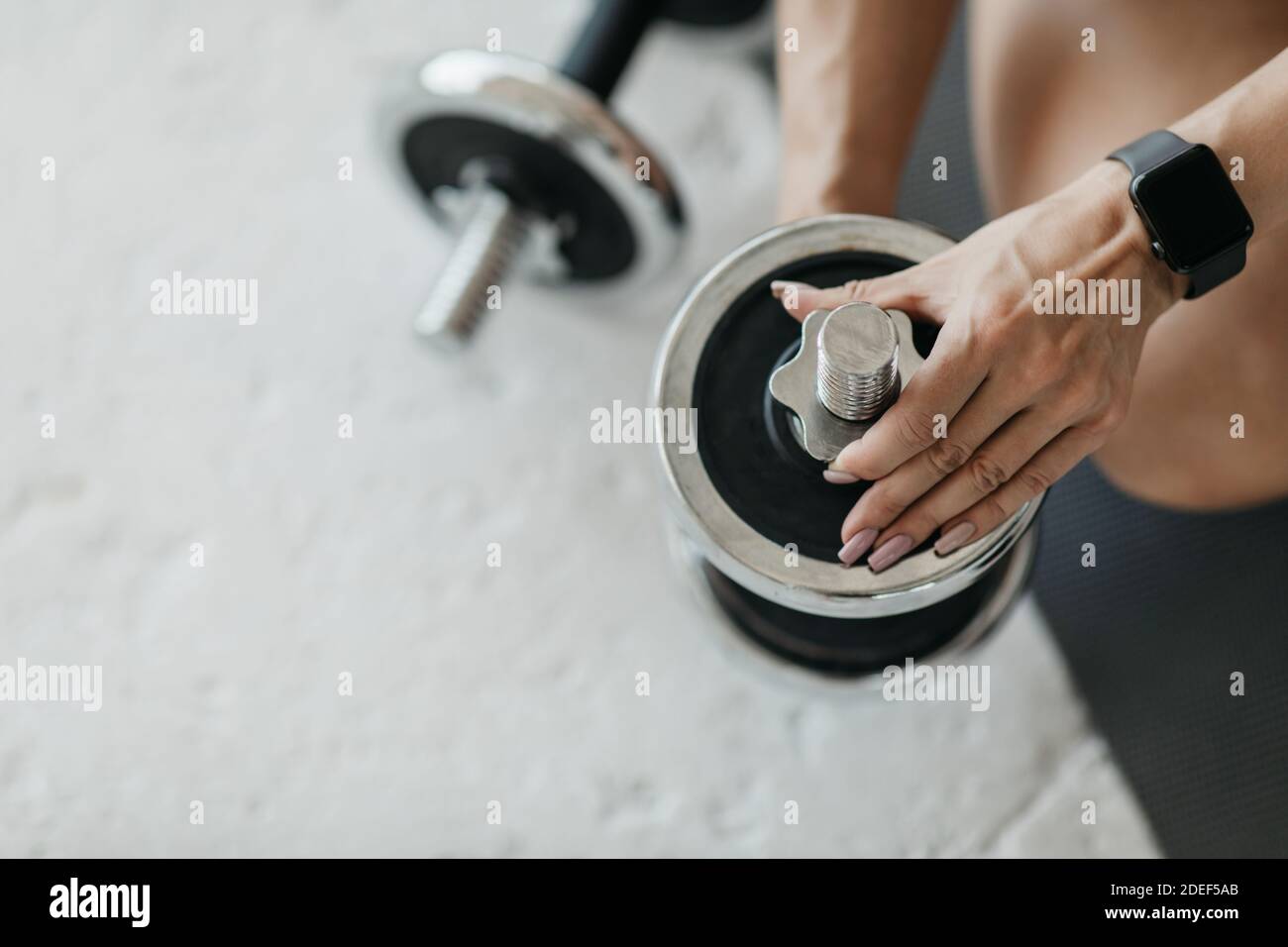 Modern technology and strength training. Middle aged woman tunes tools, changes weight on dumbbell Stock Photo