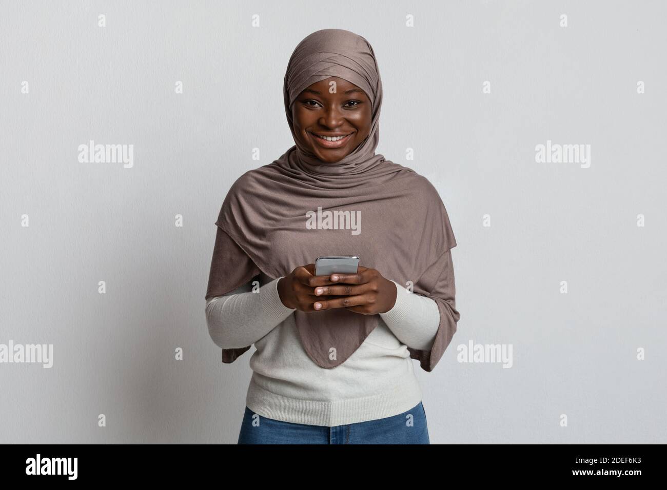 Modern Black Islamic Woman In Hijab Using Smartphone And Smiling At ...