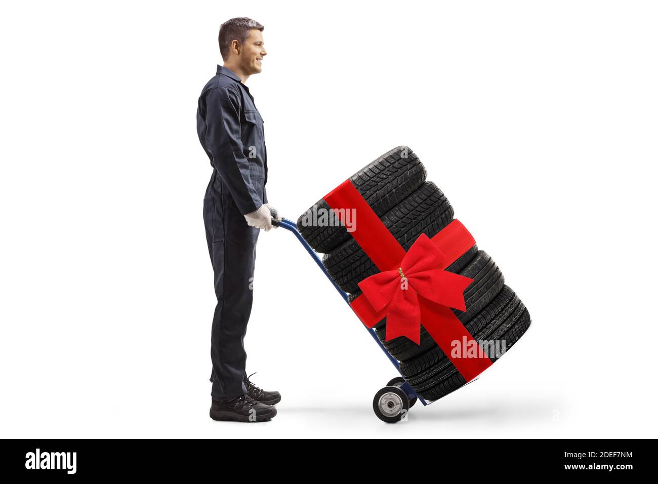 Full length profile shot of a mechanic worker pushing car tires with a red bow on a hand truck isolated on white background Stock Photo