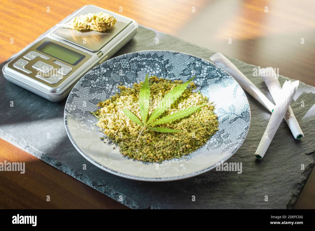 https://c8.alamy.com/comp/2DEFCDG/marijuana-joints-chopped-cannabis-and-digital-scale-on-stone-tray-with-sun-rays-2DEFCDG.jpg