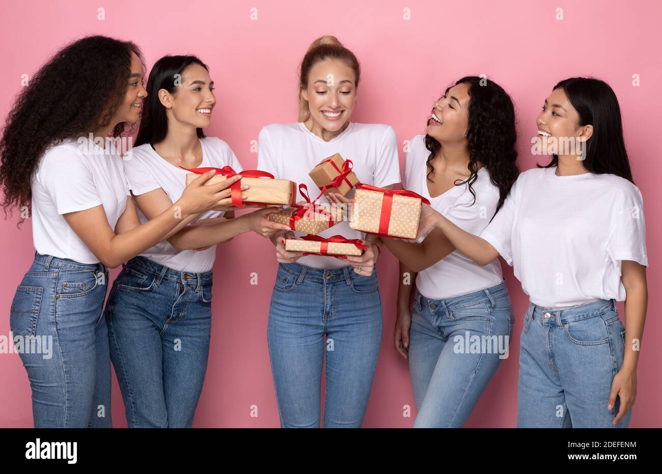 Joyful Ladies Giving Gifts Boxes To Female Friend, Pink Background Stock Photo
