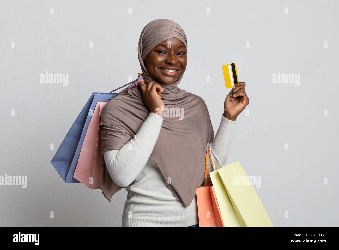 Smiling Black Muslim Woman In Hijab Holding Shopping Bags And Credit Card Stock Photo