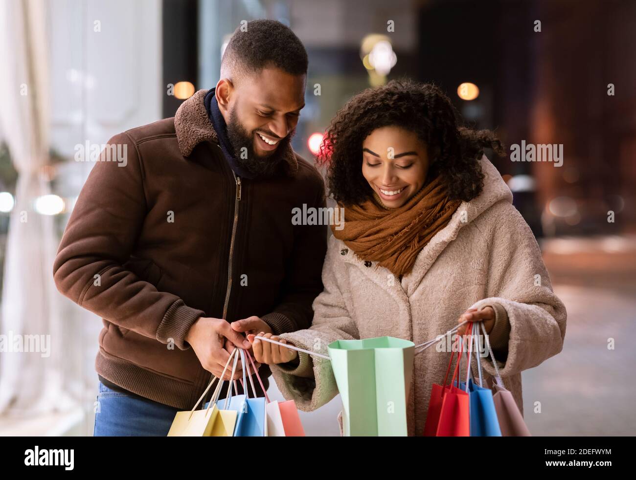 Happy black couple holding shopping bags looking inside Stock Photo - Alamy