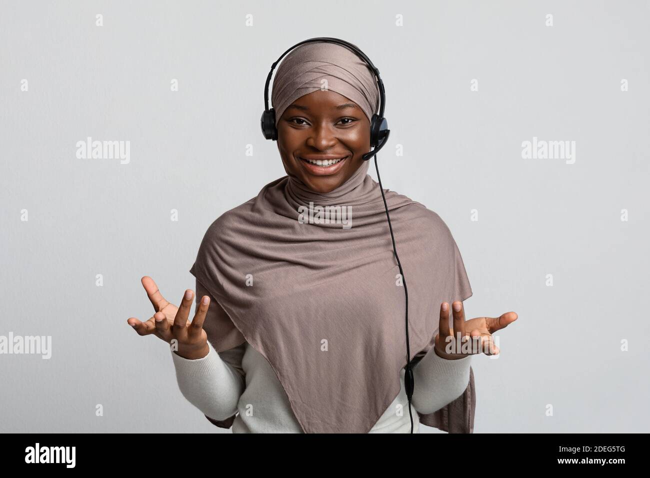 Telemarketin. Black Muslim Woman In Hijab Wearing Headset And Talking At Camera Stock Photo