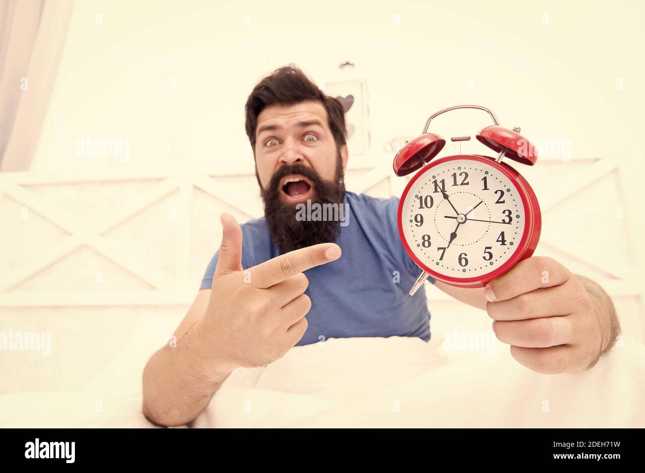 unhappy man pointing at the alarm clock. hate noise of alarm clock. Man