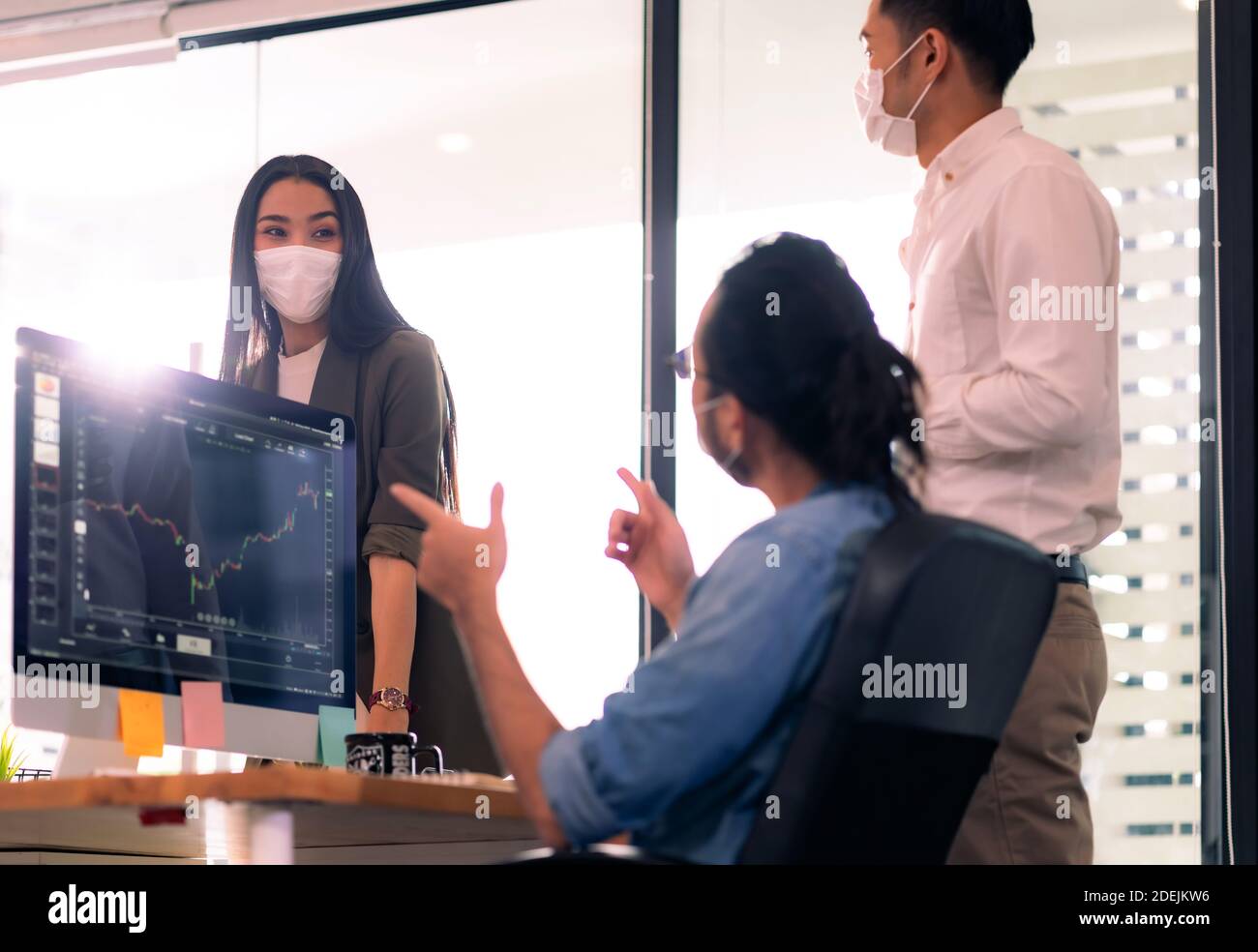 Three asian business person discuss their work in morning after office reopen due to coronavirus COVID-19 pandemic. They wear protective face mask to Stock Photo