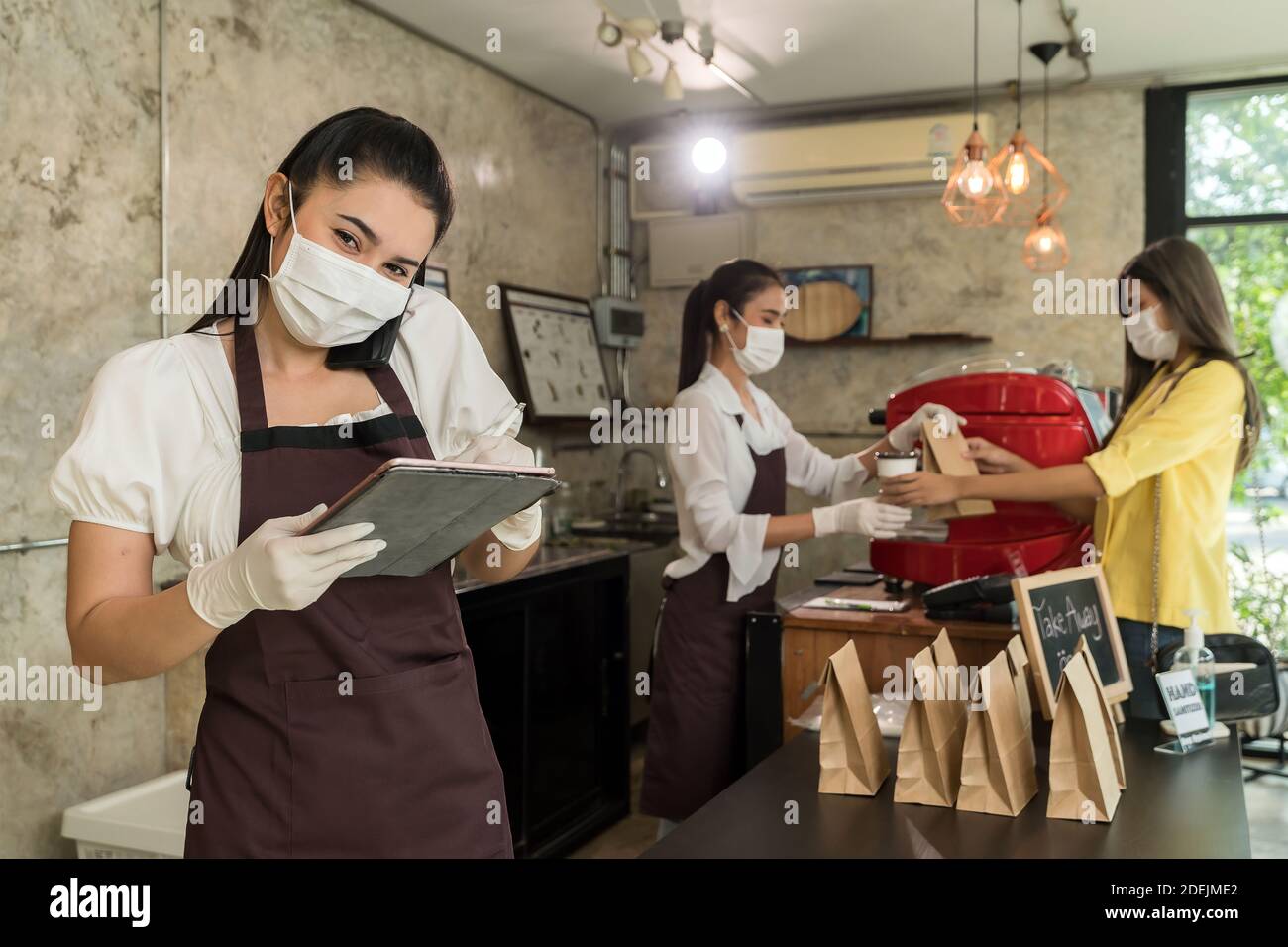 Asian waitress take order from mobile phone for takeout and curbside pickup orders while city lockdown. They wear protective face mask to prevent from Stock Photo