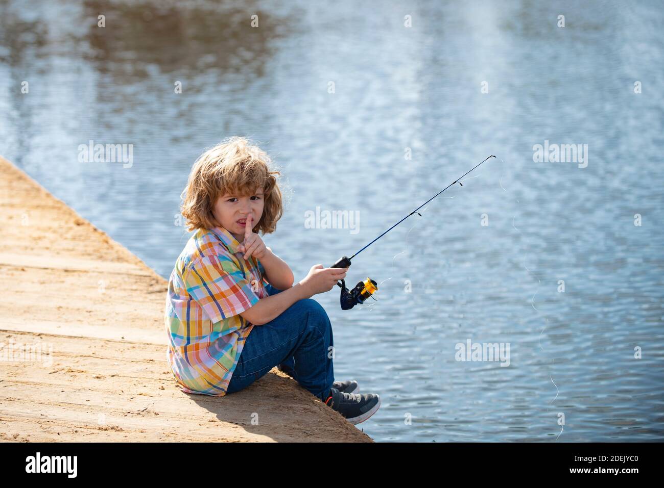 Serious, little boy child is fishing on the river with a fishing rod