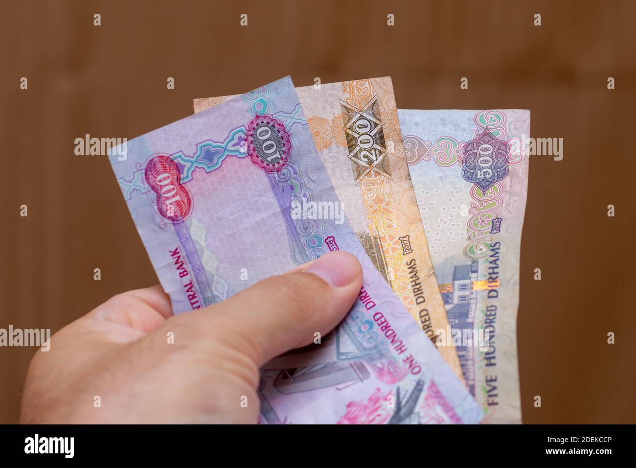 Persons hand giving the Currency of the United Arab Emirates (UAE) -  Multiple hundred Dirham notes spread out on a brown background. Money  exchange Stock Photo - Alamy