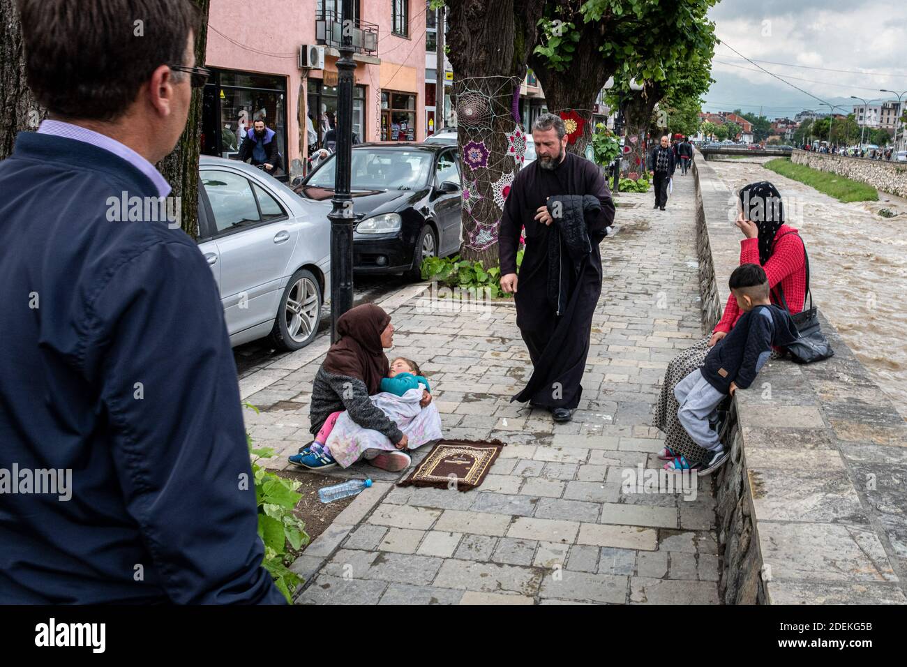 Prizren, 14 mai 2019. Sur le bord de la riviere Bistrica, le pere serdjian de Gracanica fait l'aumone à des mendiantes musulmanes, durant le mois de ramadan. Stock Photo