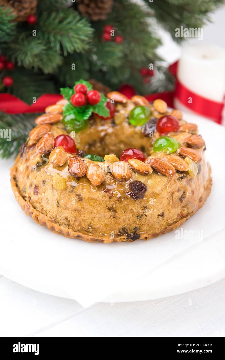 Colorful delicious homemade Christmas fruit cake on white platter with decorating items preparing for celebrating festive season Stock Photo