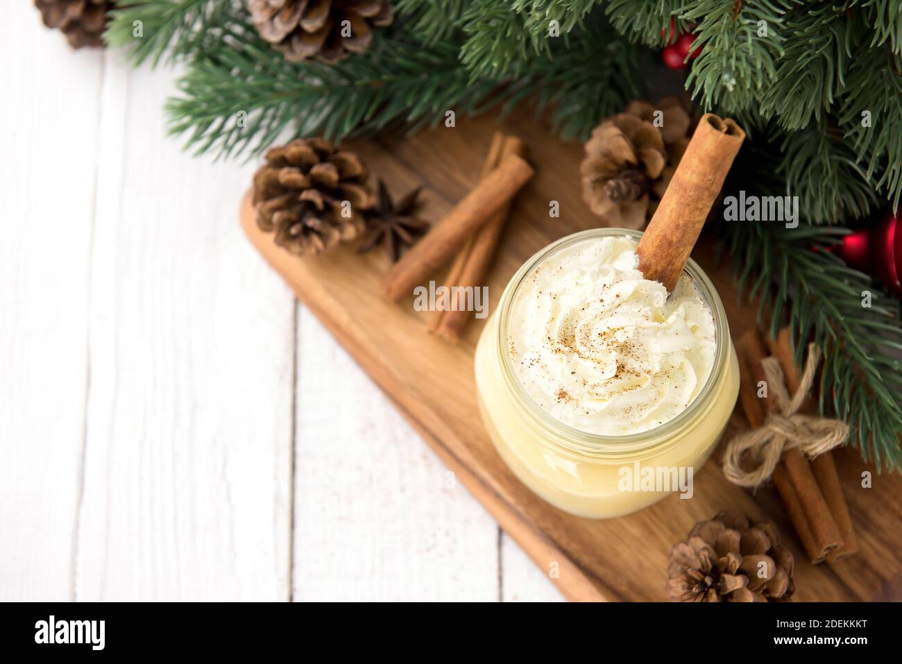 Traditional Christmas eggnog drink with whipped cream, ground nutmeg, cinnamon and decorating items on wood table, preparing for celebrating festive h Stock Photo