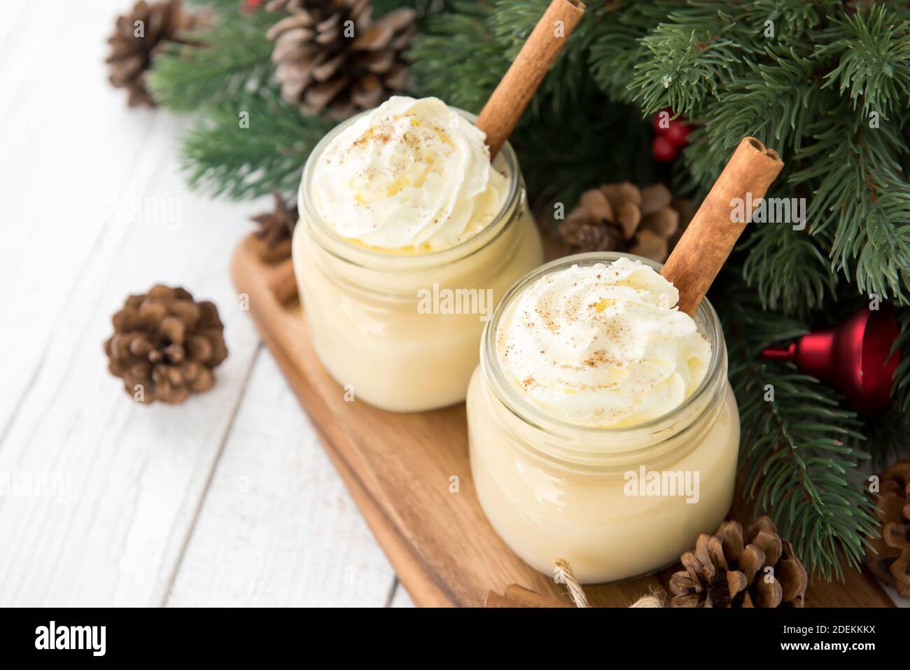 Traditional Christmas eggnog drinks with whipped cream, ground nutmeg, cinnamon and decorating items on wood table, preparing for celebrating festive Stock Photo