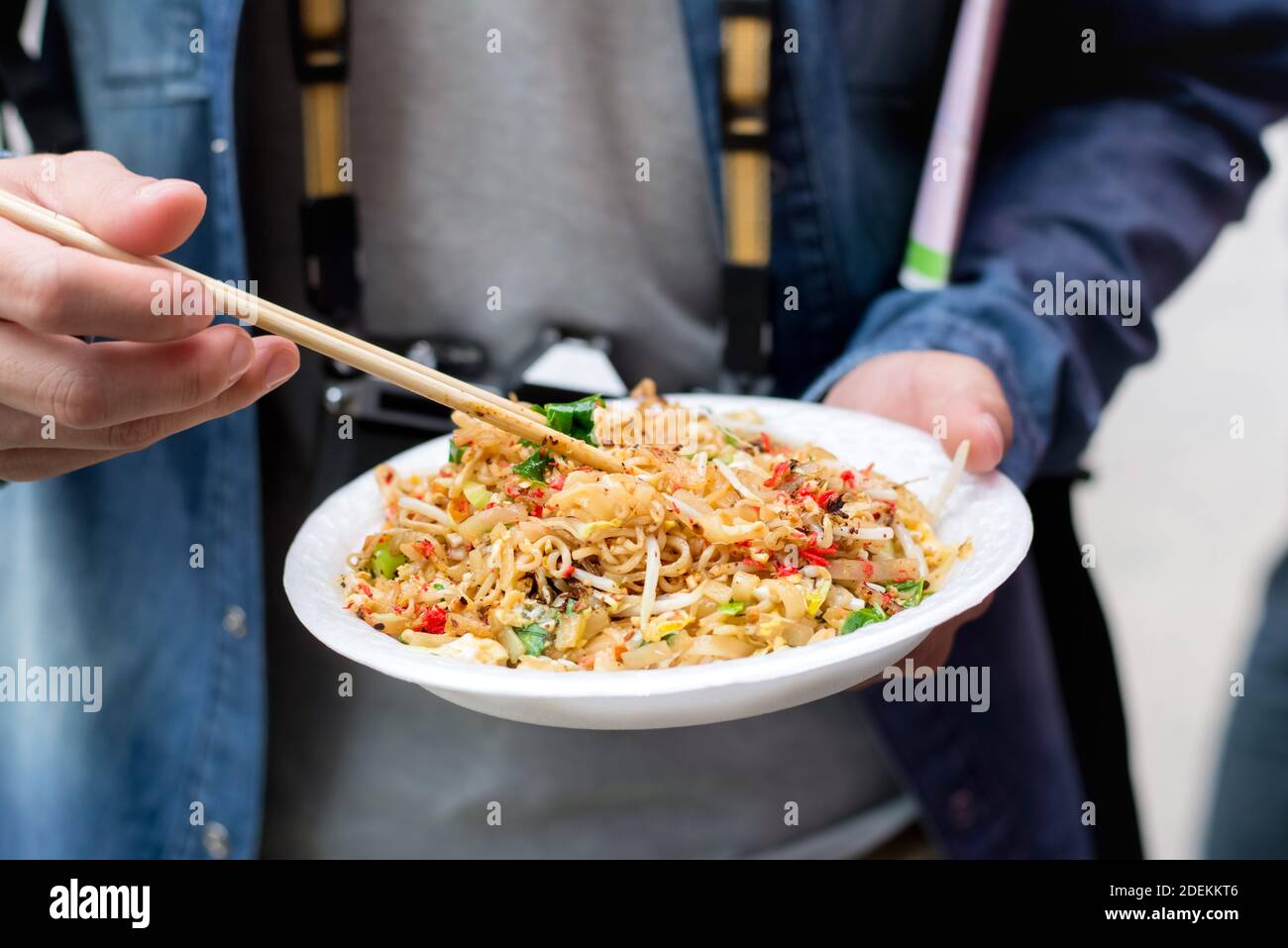 Tourist hands holding Pad Thai, one of famous traditional Thailand street food, with chopsticks about to eat while traveling in Bangkok Stock Photo
