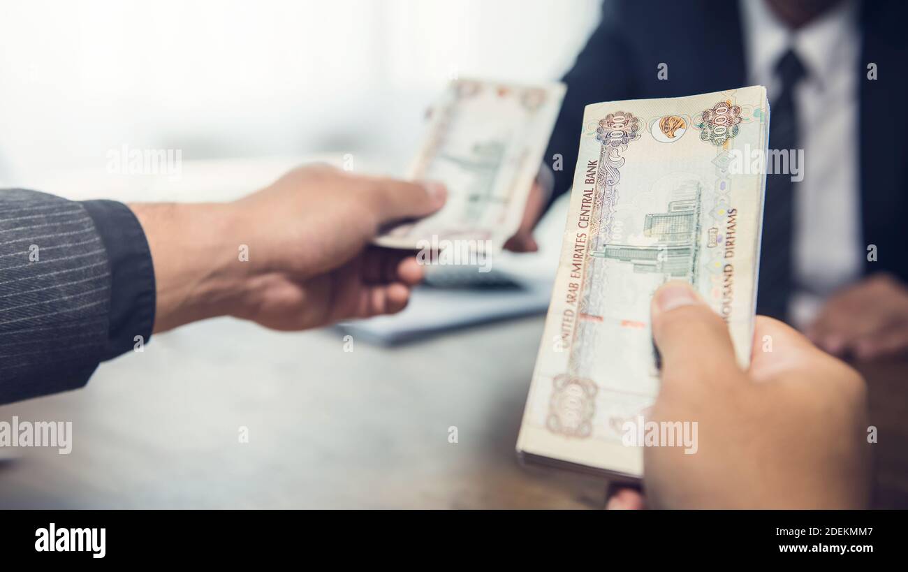 A business man giving banknote money of UAE Dirhams over a wooden table in privacy - loan, payment and bribery concept Stock Photo