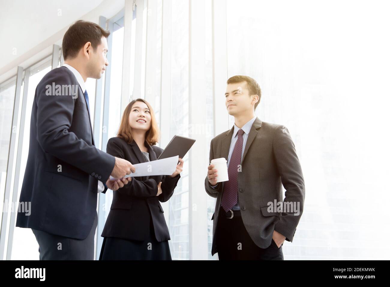Mixed group of business people standing at the office building hallway, meeting to talk and discuss work during coffee break Stock Photo