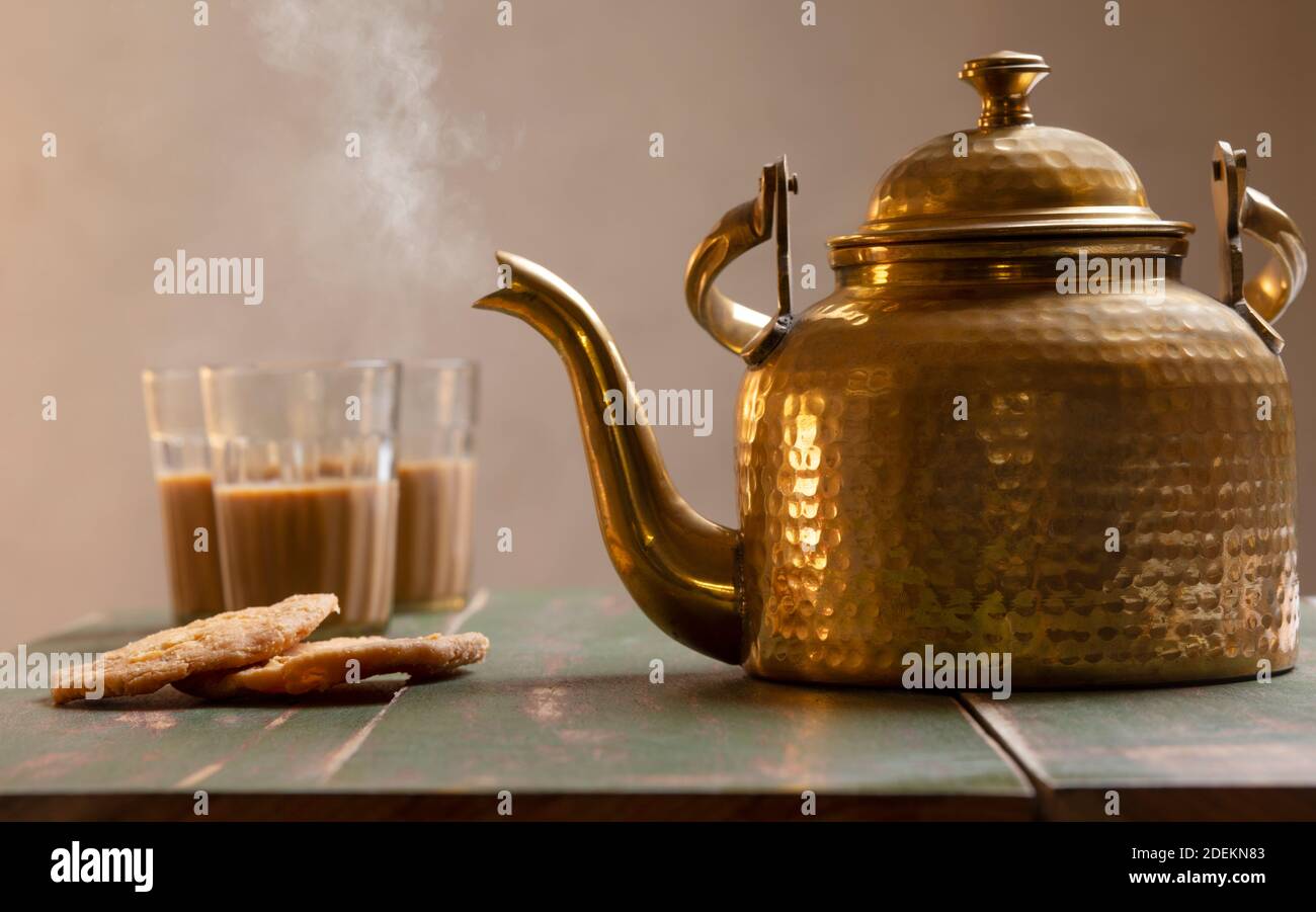 Electric kettle and tea glass on a table. Yellow curtain and brown wall in  the background Stock Photo