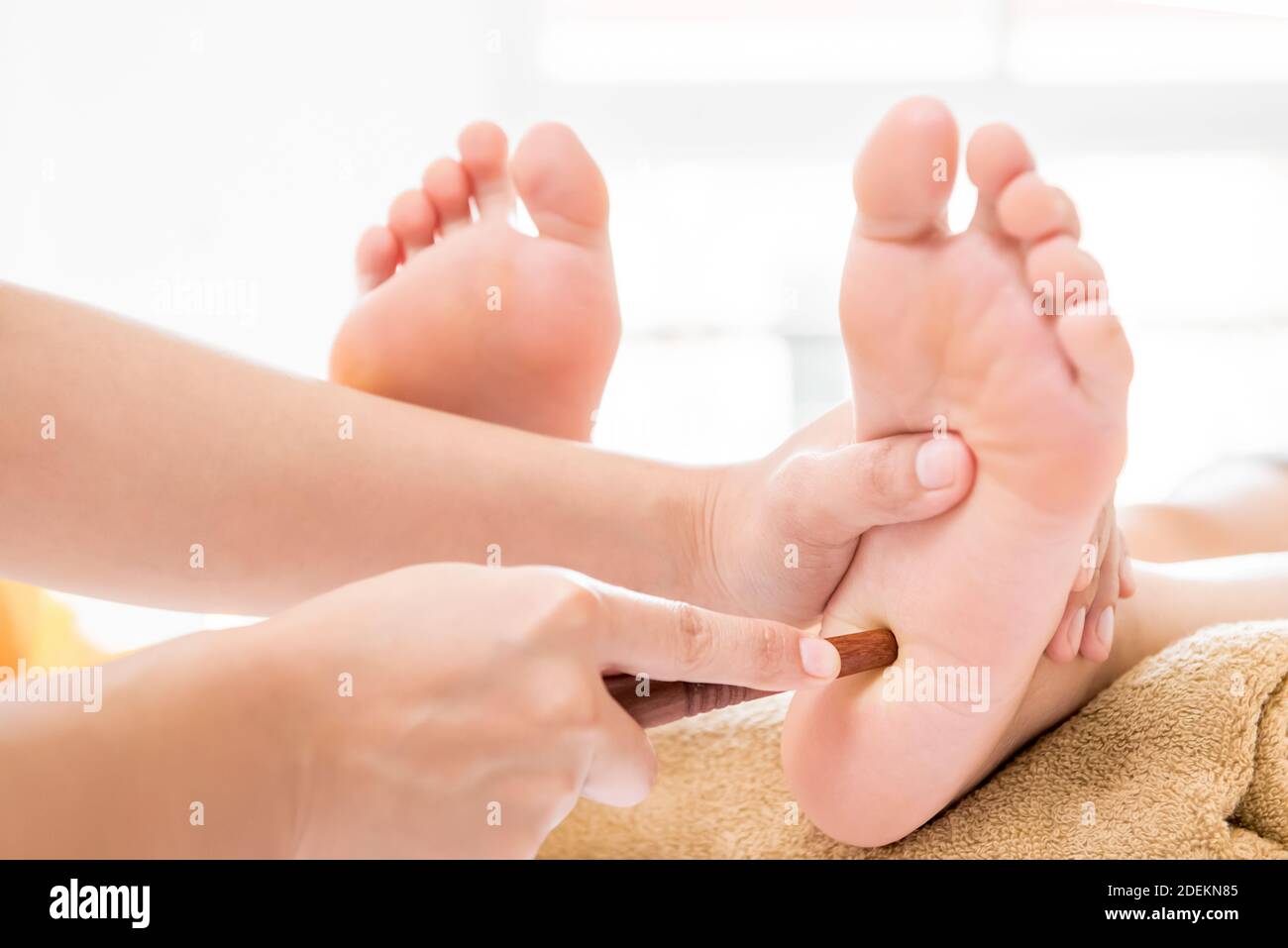 Professional therapist giving reflexology relaxing traditional Thai foot massage treatment with stick to a woman in spa Stock Photo