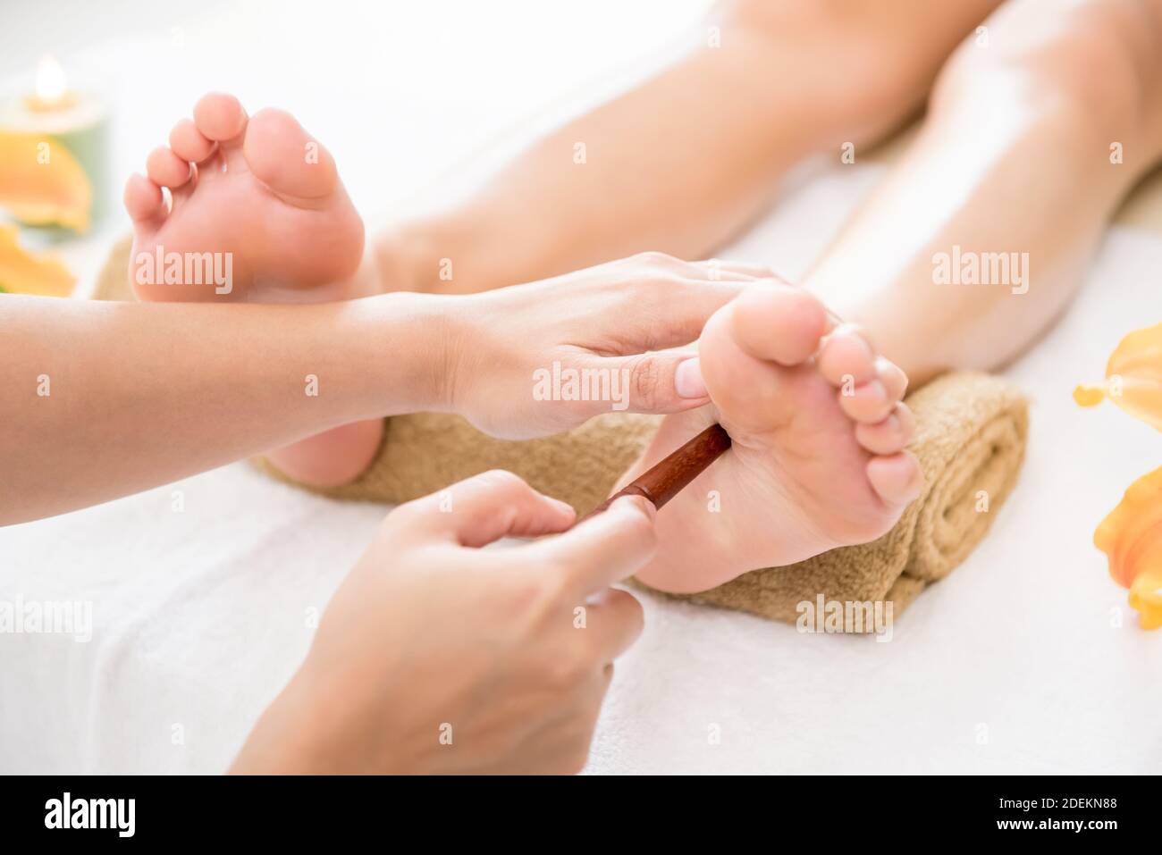 Professional therapist giving reflexology relaxing traditional Thai foot massage treatment with stick to a woman in spa Stock Photo