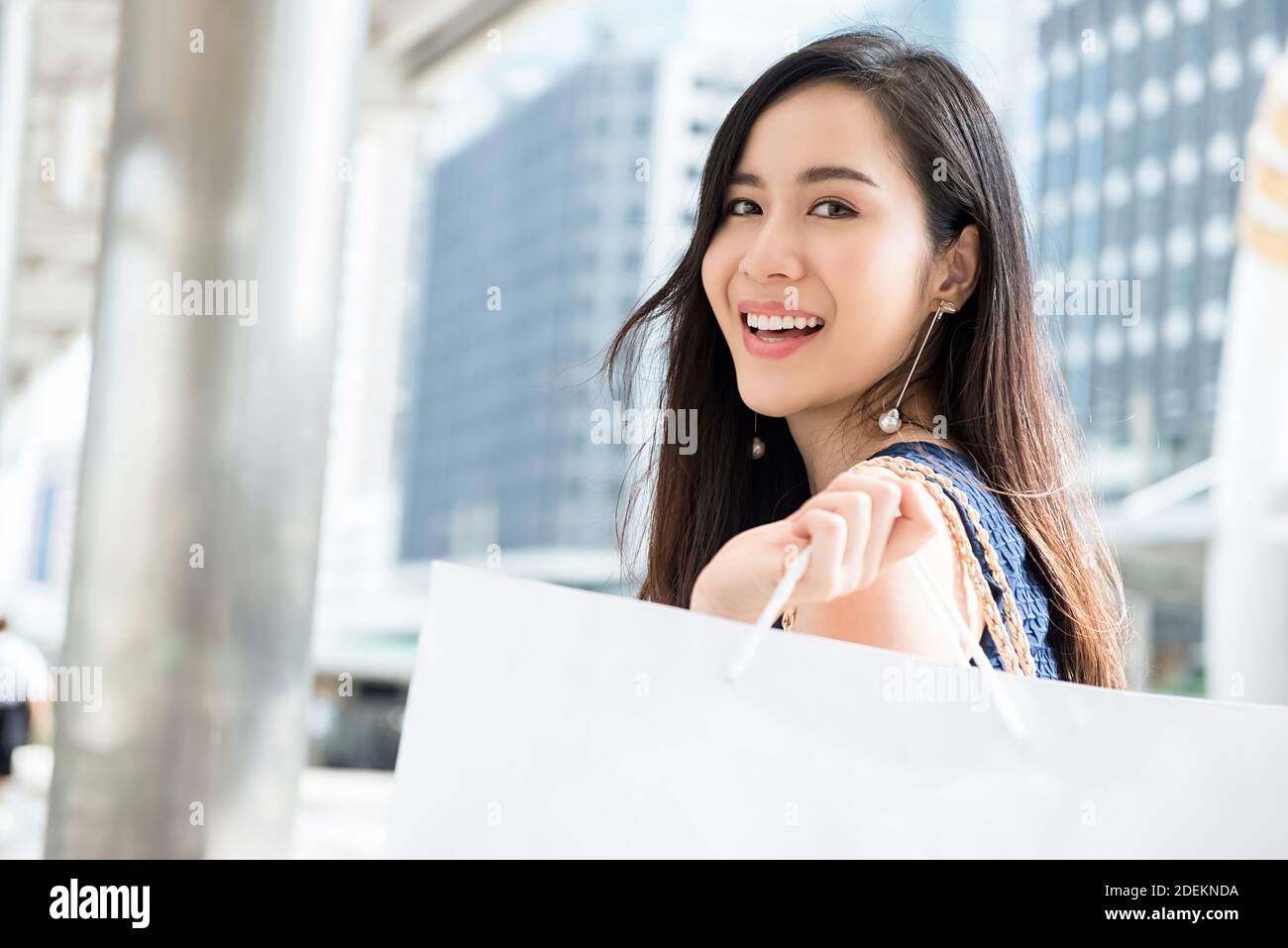 Beautiful young Asian woman carrying bag enjoying her time in the city after shopping during holiday sales season Stock Photo